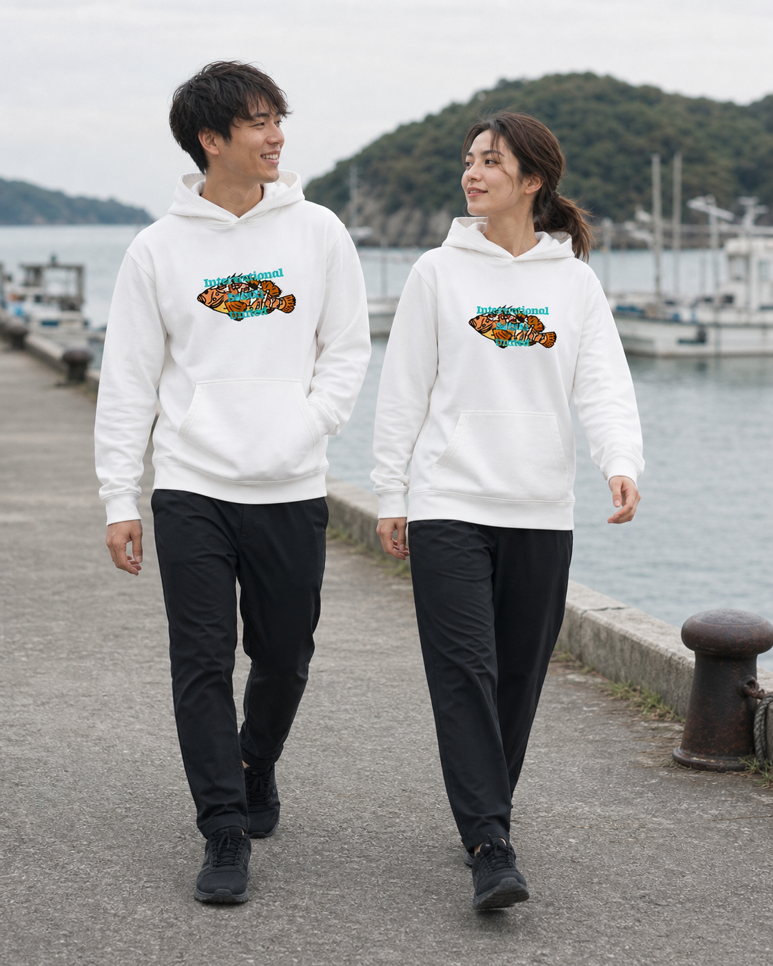 白いISU AKOUパーカーを着て、港を歩きながら会話する男性と女性