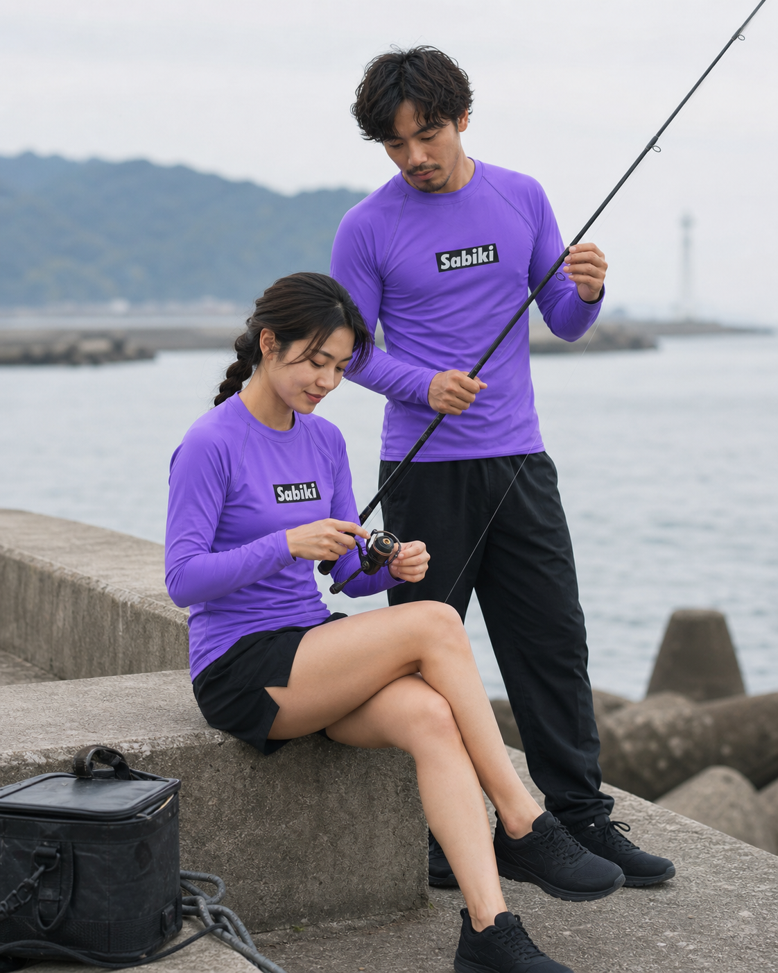 紫のSABIKIラッシュガードを着て、リールの糸を整える女性とロッドを支える男性