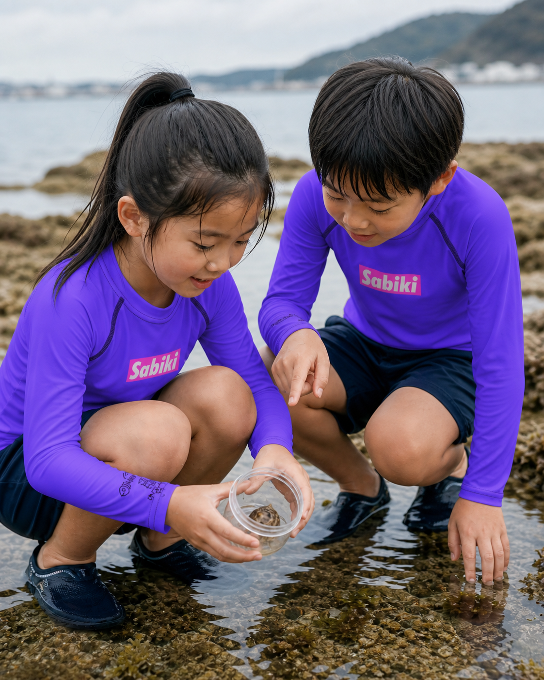 紫のSABIKI BOXキッズラッシュガードを着て潮だまりを観察する女の子と男の子