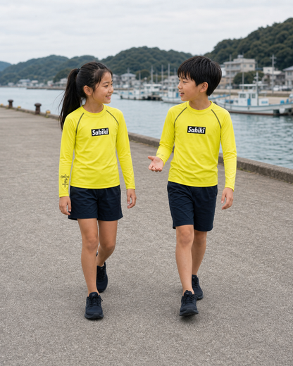 ネオンイエローのSABIKI BOXキッズラッシュガードを着て港を歩く女の子と男の子