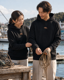 Sudadera con capucha unisex ISU AKOU | Diseño de un punto en el pechoを港で着用する男性と女性