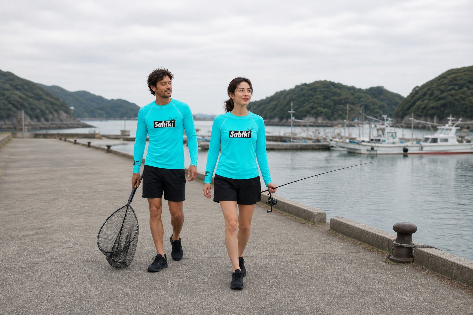 ターコイズのSABIKIラッシュガードを着て港を歩く男性と女性